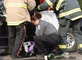 Two EMTs and a fireman work quickly to monitor and free a trapped auto accident victim.